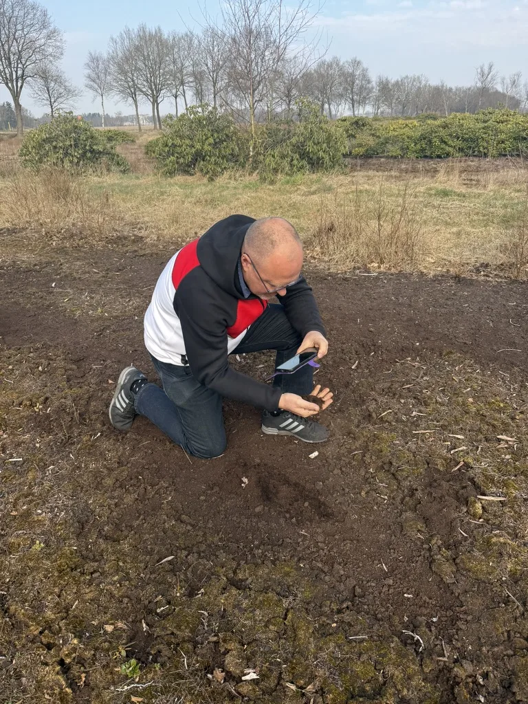 Doug McMillan kniet auf entwässertem Moorboden und fotografiert eine Bodenprobe in seiner Hand