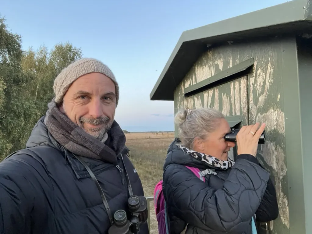 Zwei Personen an einer Beobachtungshütte, eine schaut durchs Fernglas