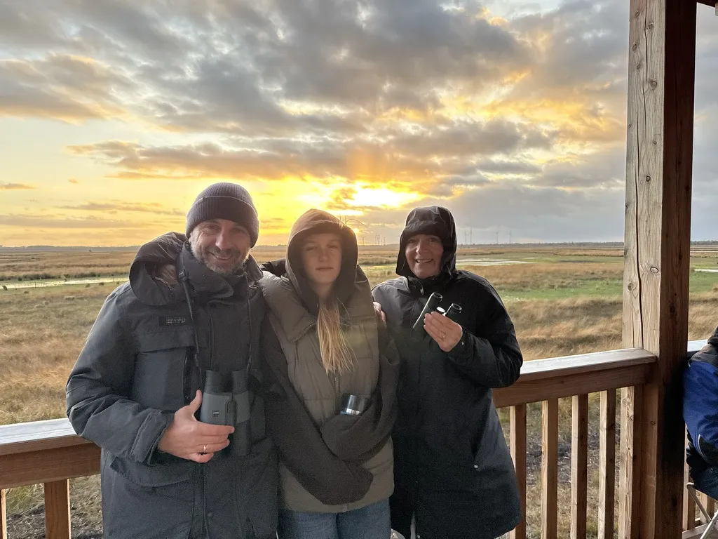 Drei Personen mit Ferngläsern auf einem Aussichtsturm im Abendlicht