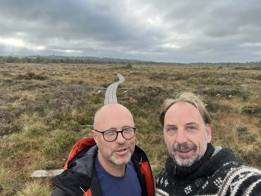 Zwei Männer im Selfie vor einem Bohlensteg im Hochmoor